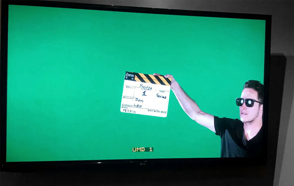A production monitor showing the green-screen feed — a crew member in sunglasses holds the Bodog clapperboard slate