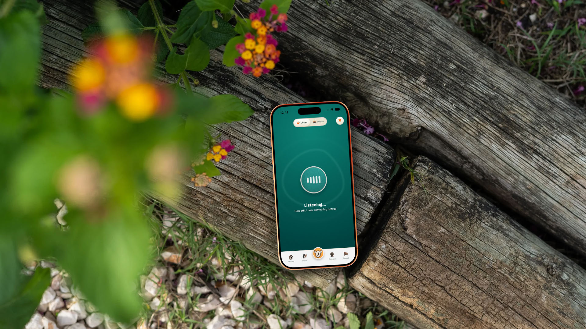 A phone resting on a weathered log among flowers, Spotter listening on its teal screen